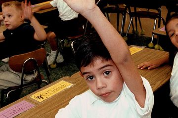 Children in classroom with hands raised
