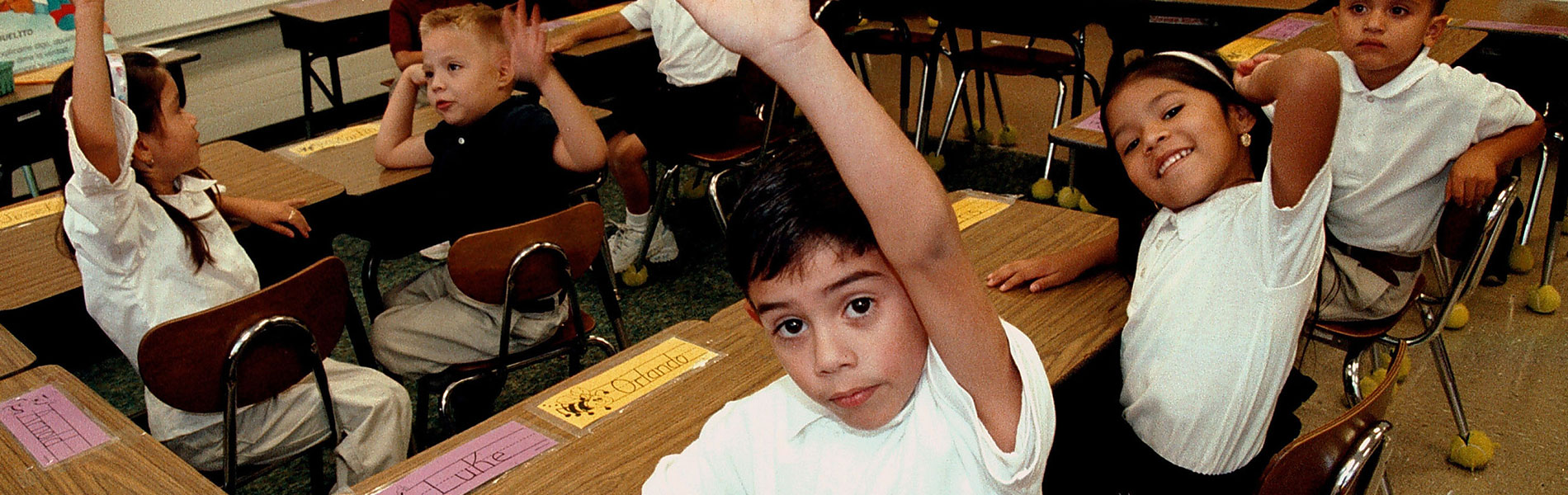 Children in classroom with hands raised