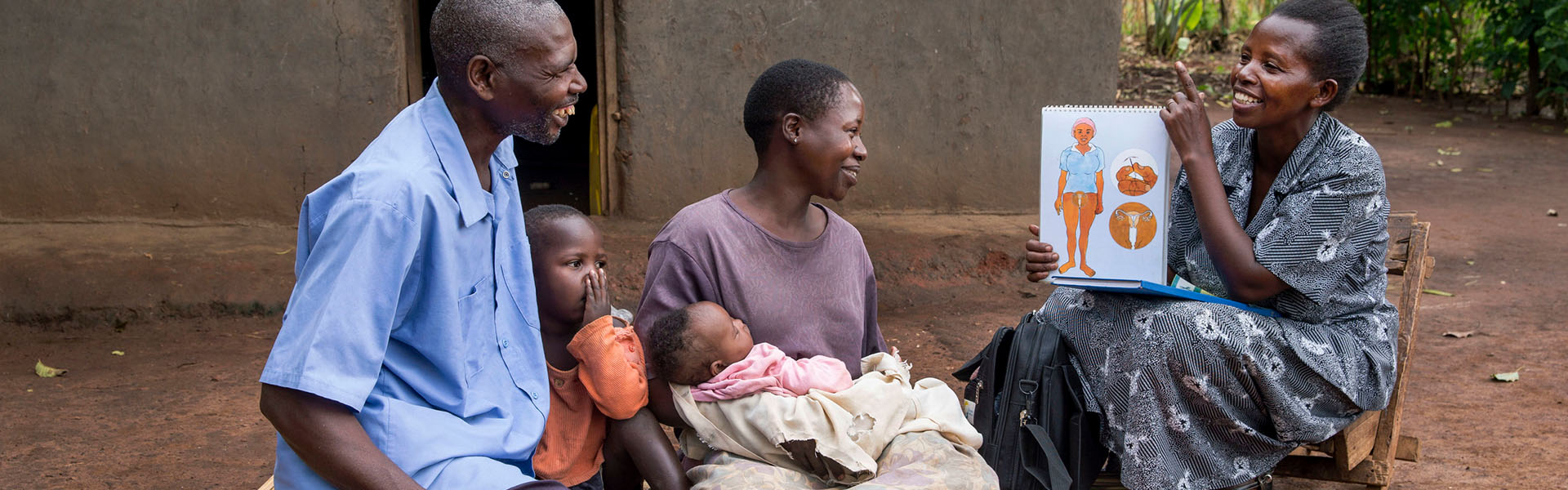 Family seated on ground outside of a home discussing family planning.