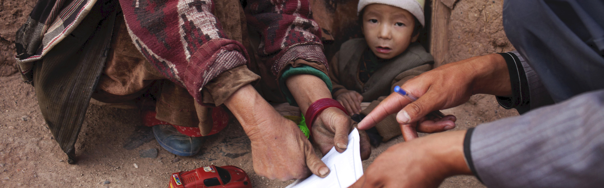 A small child looks at the camera while adults are being thumbprinted to vote in the census