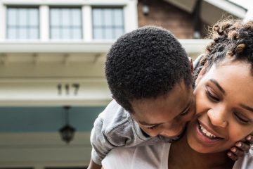 Single mother playing with young sons in front of house