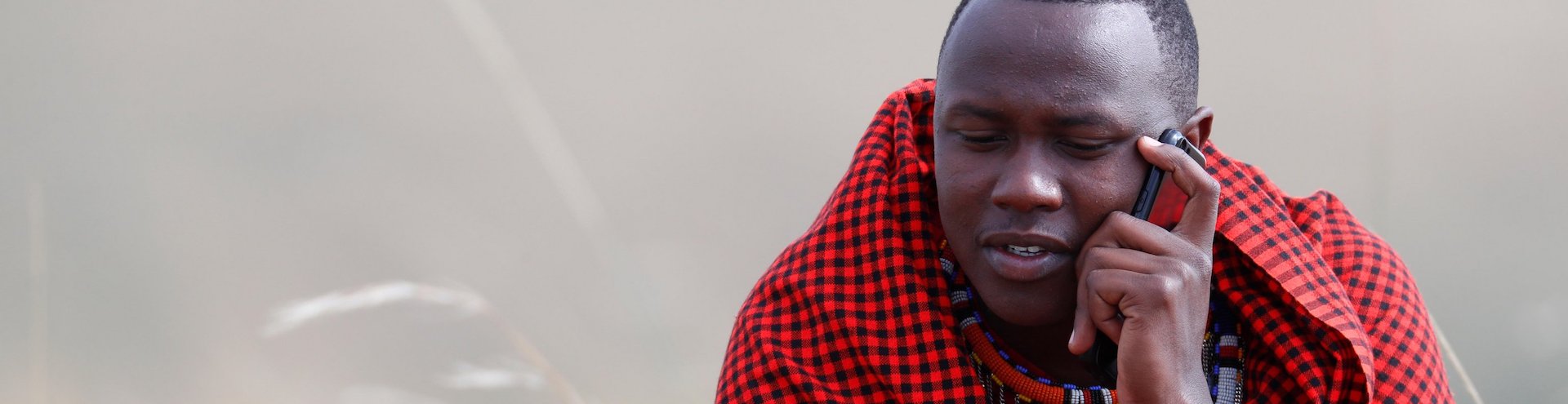 A Masai man talking on a mobile phone in the African savanna, Masai Mara Game Reserve. Kenya, East Africa, Africa