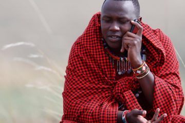 A Masai man talking on a mobile phone in the African savanna, Masai Mara Game Reserve. Kenya, East Africa, Africa