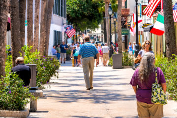 Senior couple walking by St George street sidewalk stores shops, restaurants in downtown old town of Florida city in summer