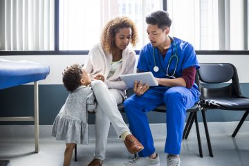 Male nurse showing digital tablet to mother by toddler in hospital