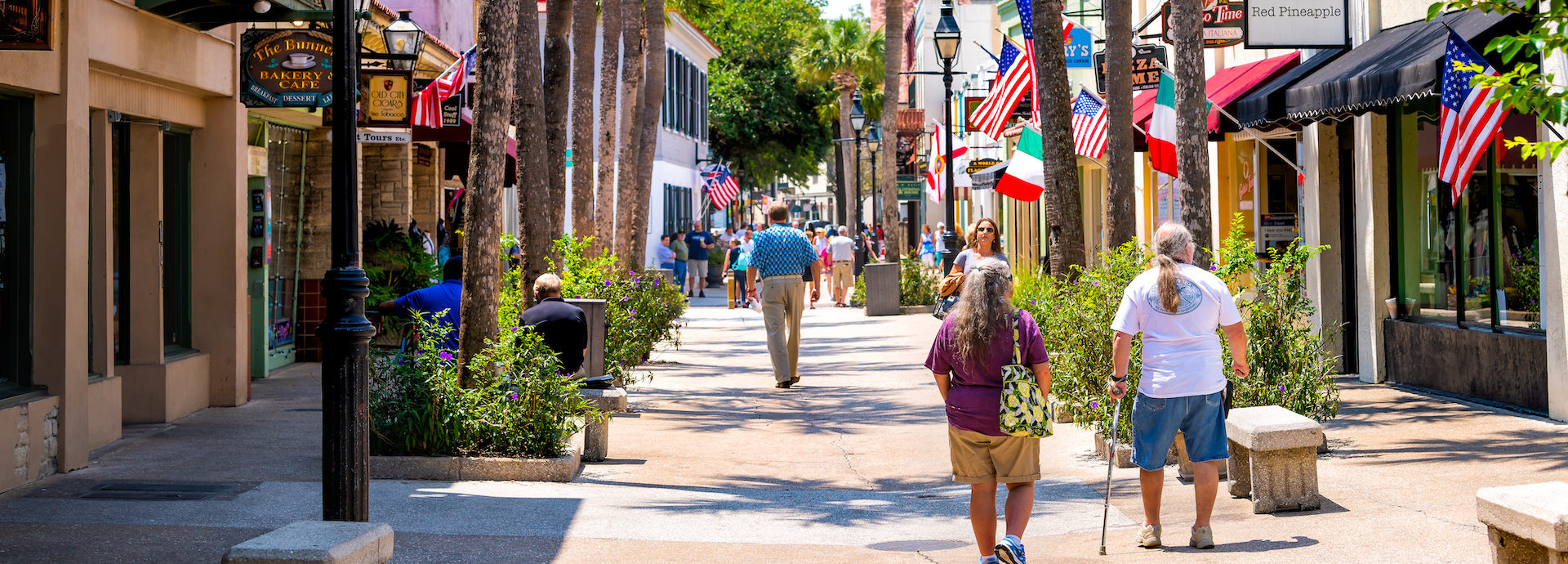 Senior couple walking by St George street sidewalk stores shops, restaurants in downtown old town of Florida city in summer