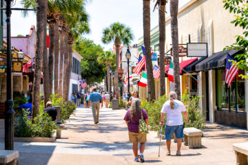 Senior couple walking by St George street sidewalk stores shops, restaurants in downtown old town of Florida city in summer