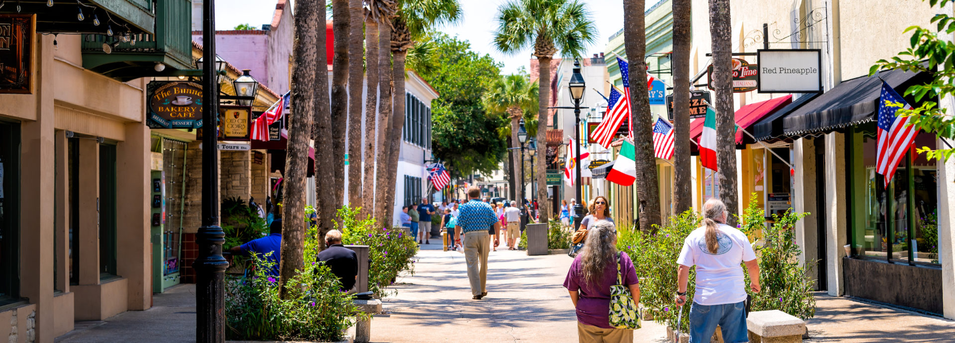 Senior couple walking by St George street sidewalk stores shops, restaurants in downtown old town of Florida city in summer