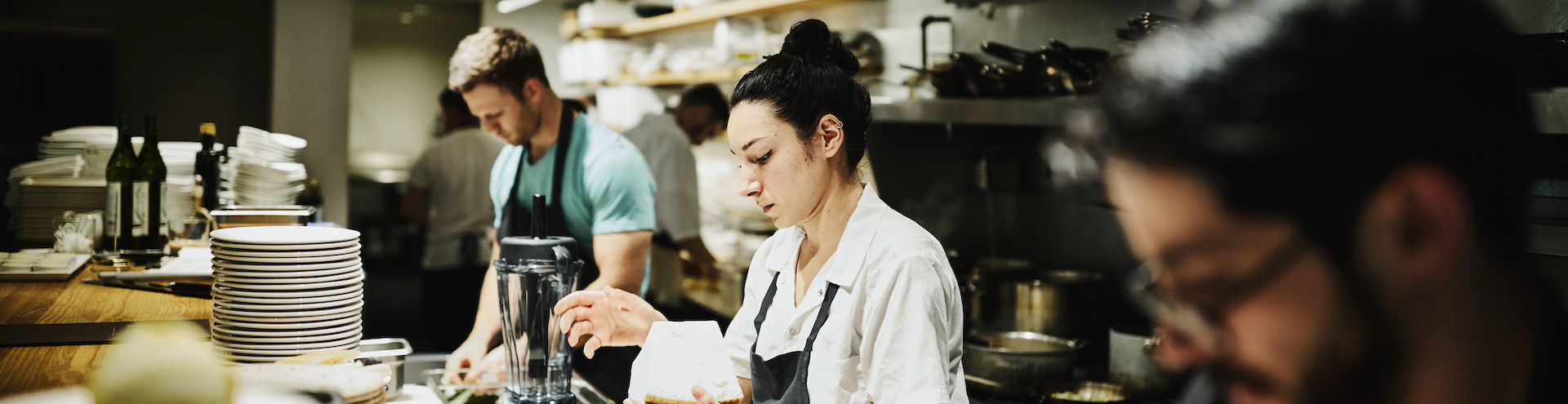 Female chef working with block of Parmesan cheese while preparing for dinner service in restaurant kitchen