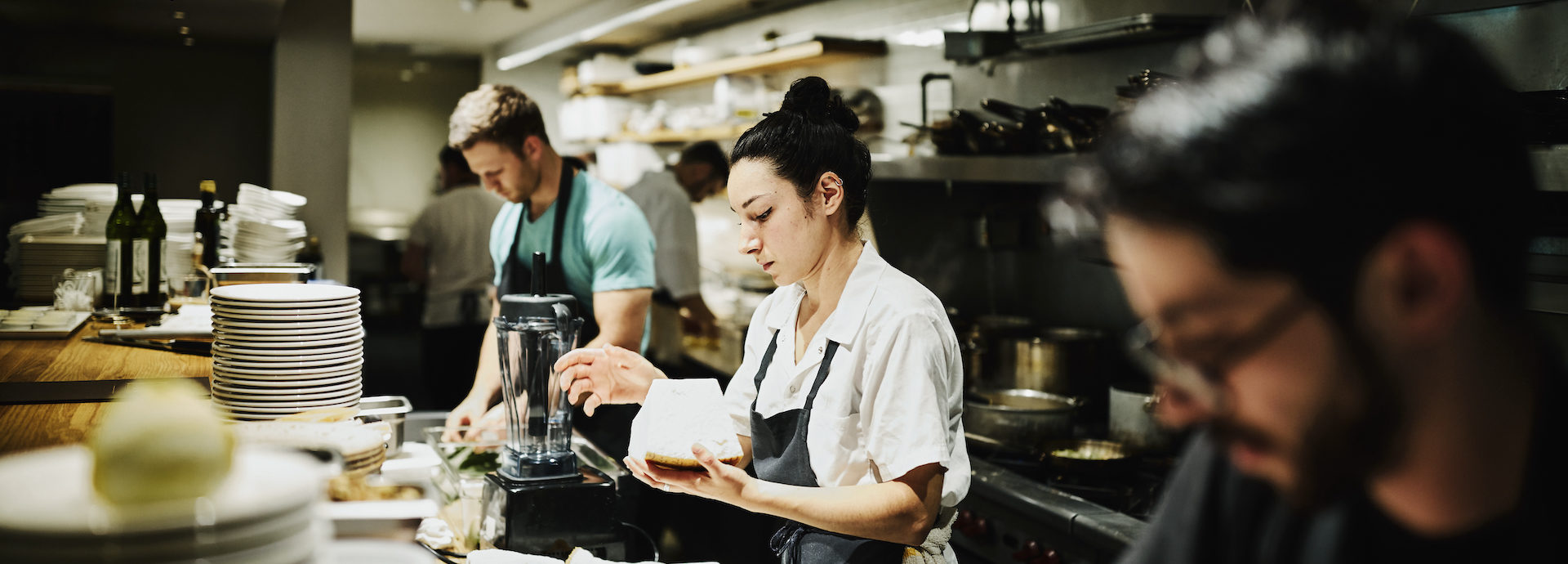 Female chef working with block of Parmesan cheese while preparing for dinner service in restaurant kitchen
