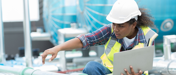 Female engineer working with laptop computer for checks or maintenance in sewer pipes area at construction site. African American woman engineer working in sewer pipes area at rooftop of building