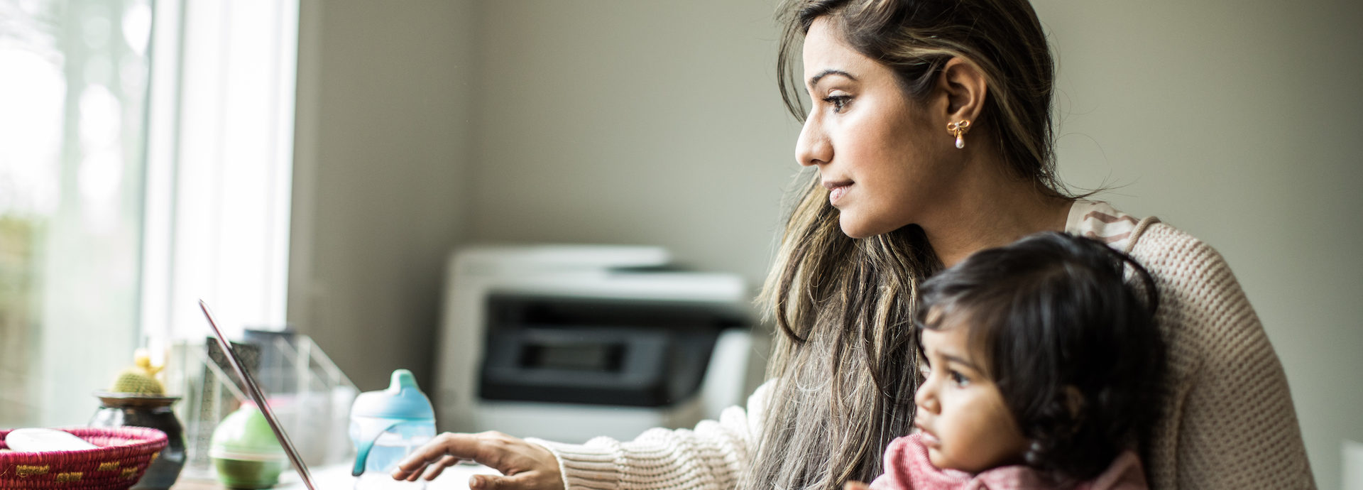 Mother multi-tasking with infant daughter in home office