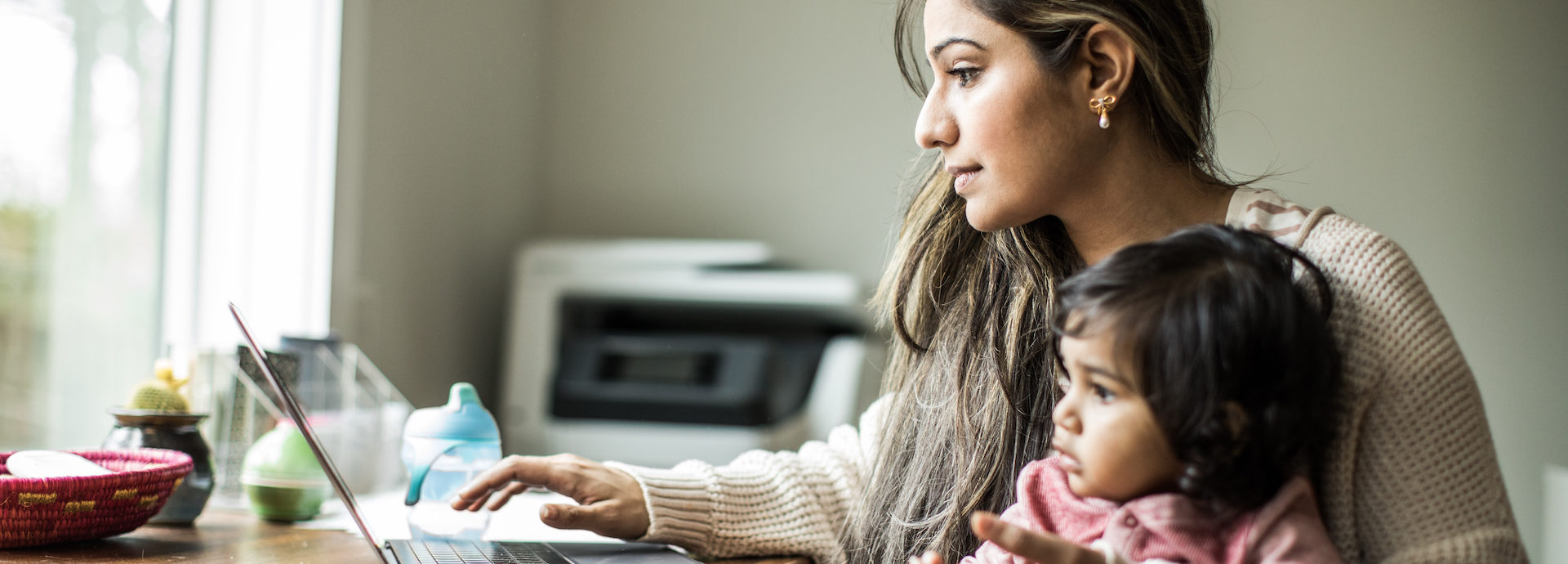Mother multi-tasking with infant daughter in home office