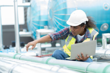 Female engineer working with laptop computer for checks or maintenance in sewer pipes area at construction site. African American woman engineer working in sewer pipes area at rooftop of building