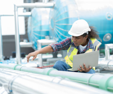 Female engineer working with laptop computer for checks or maintenance in sewer pipes area at construction site. African American woman engineer working in sewer pipes area at rooftop of building