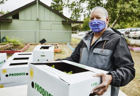 Senior man wearing protective face mask that says vote while carrying CSA box at community center