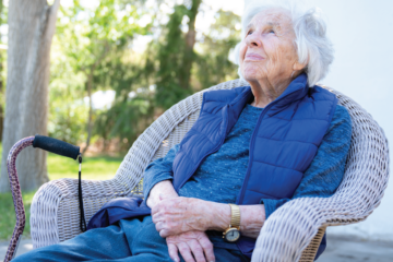 An elderly woman sits outside her home