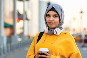 A young muslim American woman holds coffee in a city street.